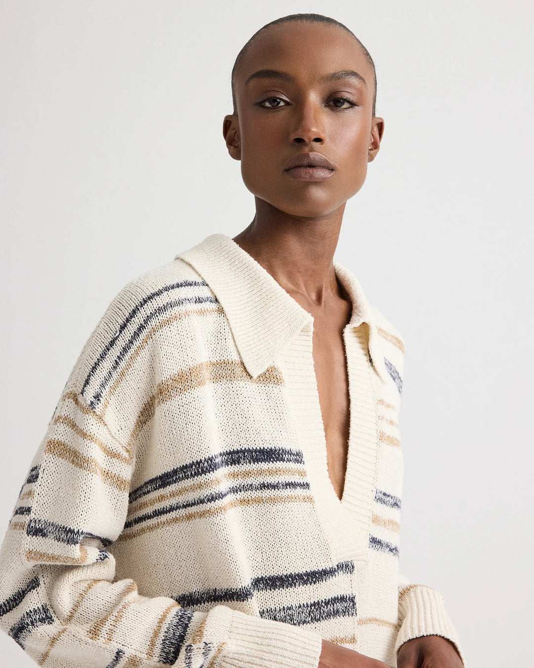 Woman wearing a cream-colored cardigan with blue and brown stripes on a white background