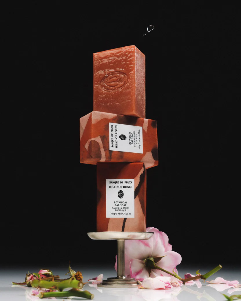Reddish-brown soap bar with a label on a stand, surrounded by flowers on a dark background