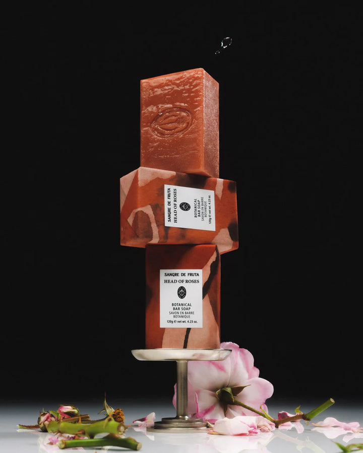 Reddish-brown soap bar with a label on a stand, surrounded by flowers on a dark background