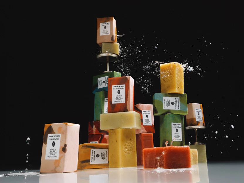 Stack of various colored soap bars on a reflective surface with a black background