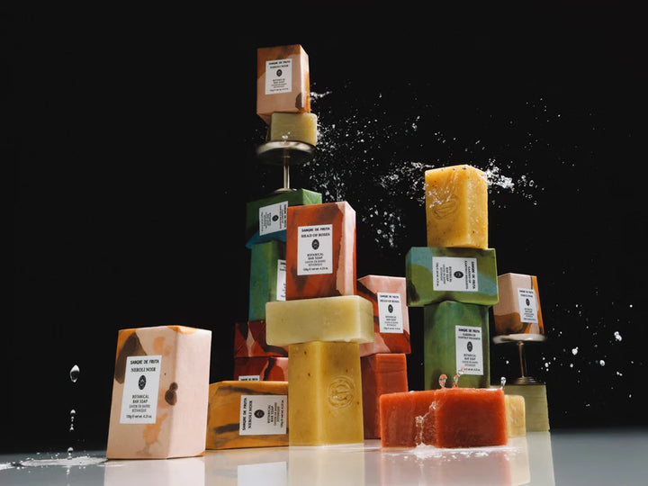 Stack of various colored soap bars on a reflective surface with a black background