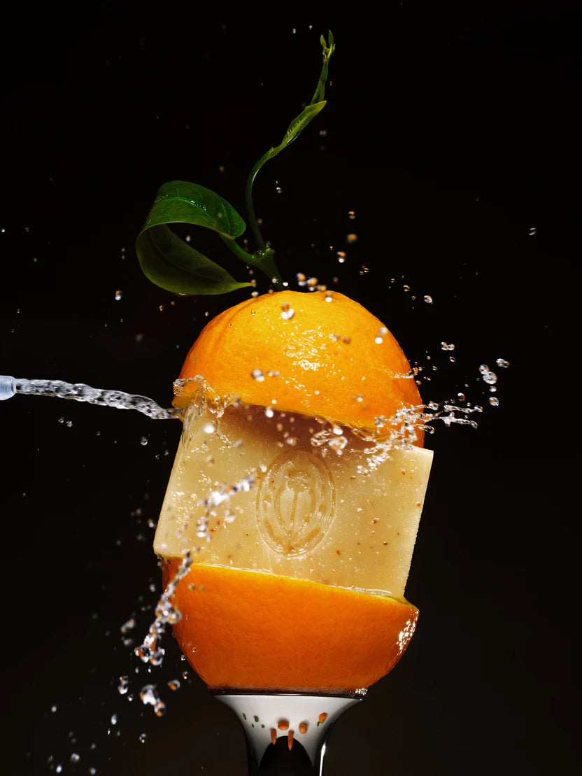 Orange being juiced with water splashing out on a black background