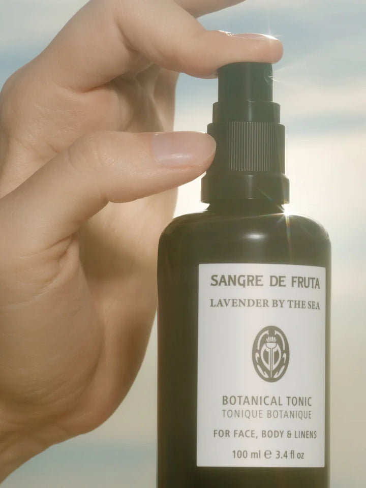 Hand holding a bottle of 'Sangre de Fruta' botanical tonic with a blurred natural background
