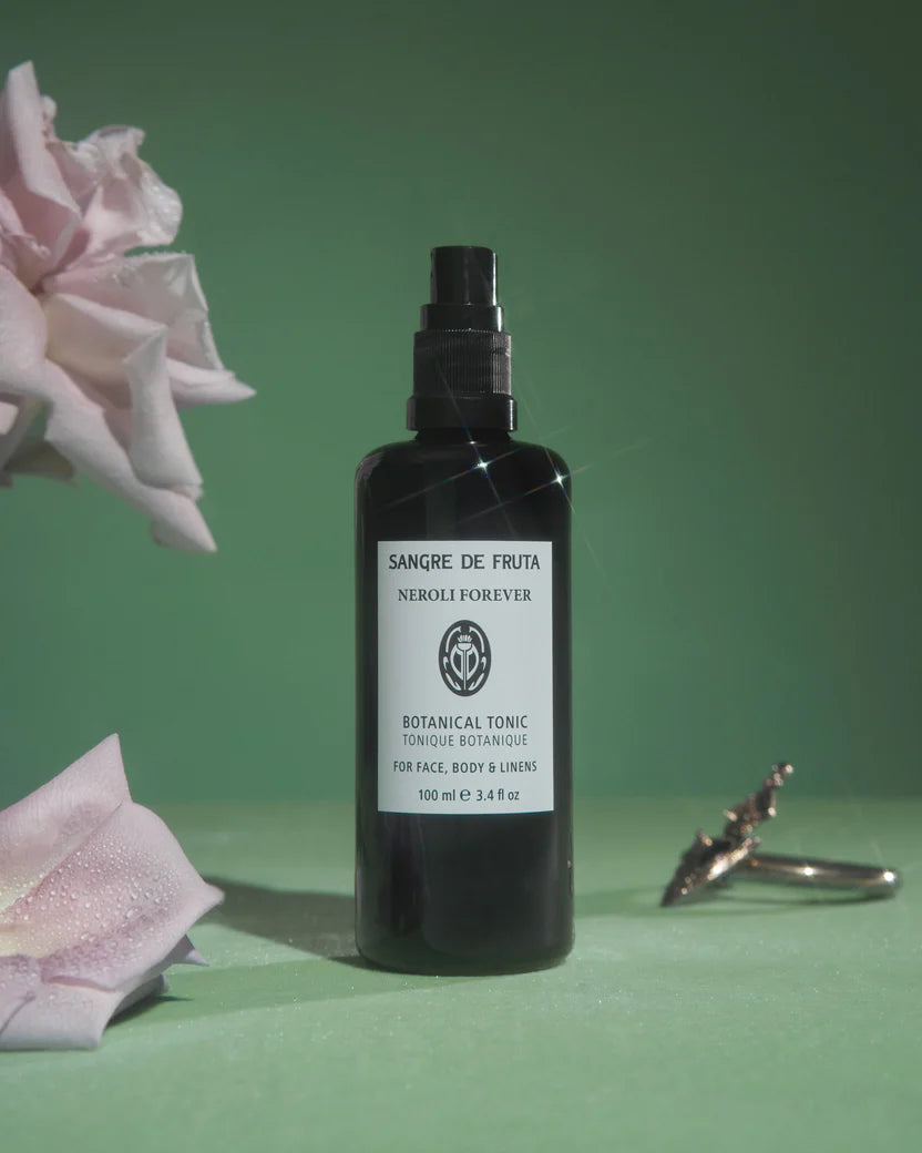 Black bottle with white label on a green background with pink flowers and a ring.