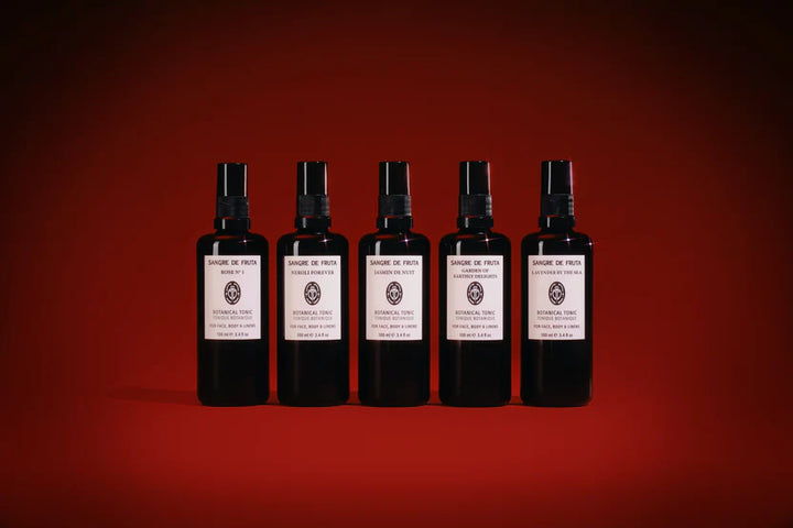 Five black spray bottles with white labels on a red background