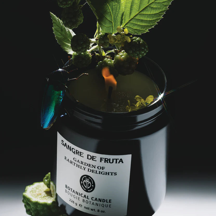 Botanical candle labeled 'Sangre de Fruta' with natural elements on a dark background