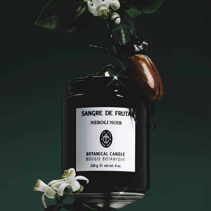 Botanical candle labeled 'Sangre de Fruta Neroli Noir' with flowers on a dark background