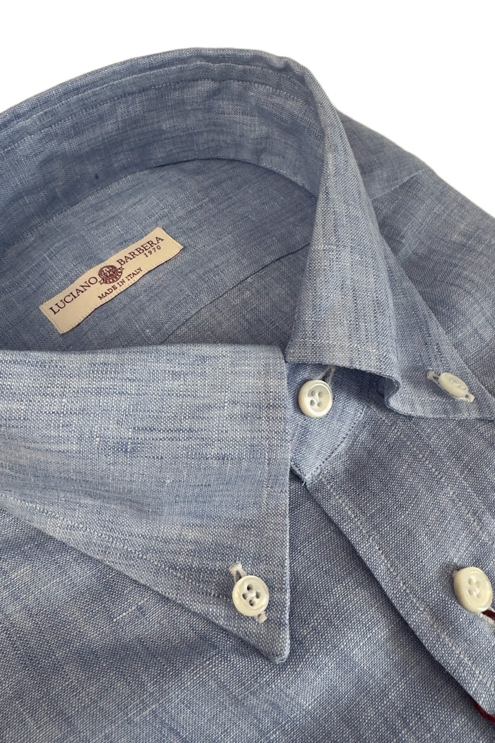 Close-up of a blue shirt with buttons and a brand label on a white background