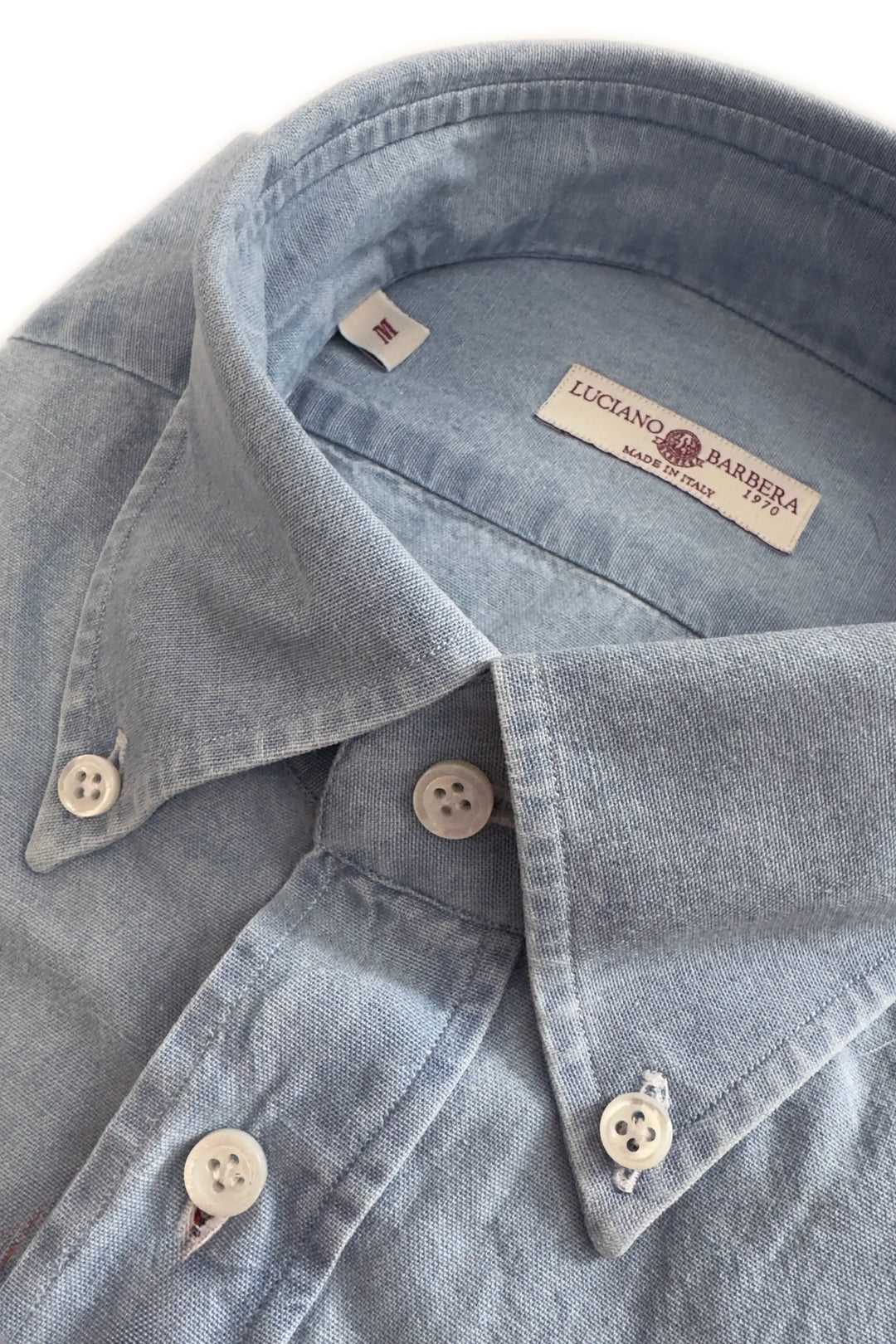 Close-up of a light blue denim shirt with buttons and a brand label on a white background