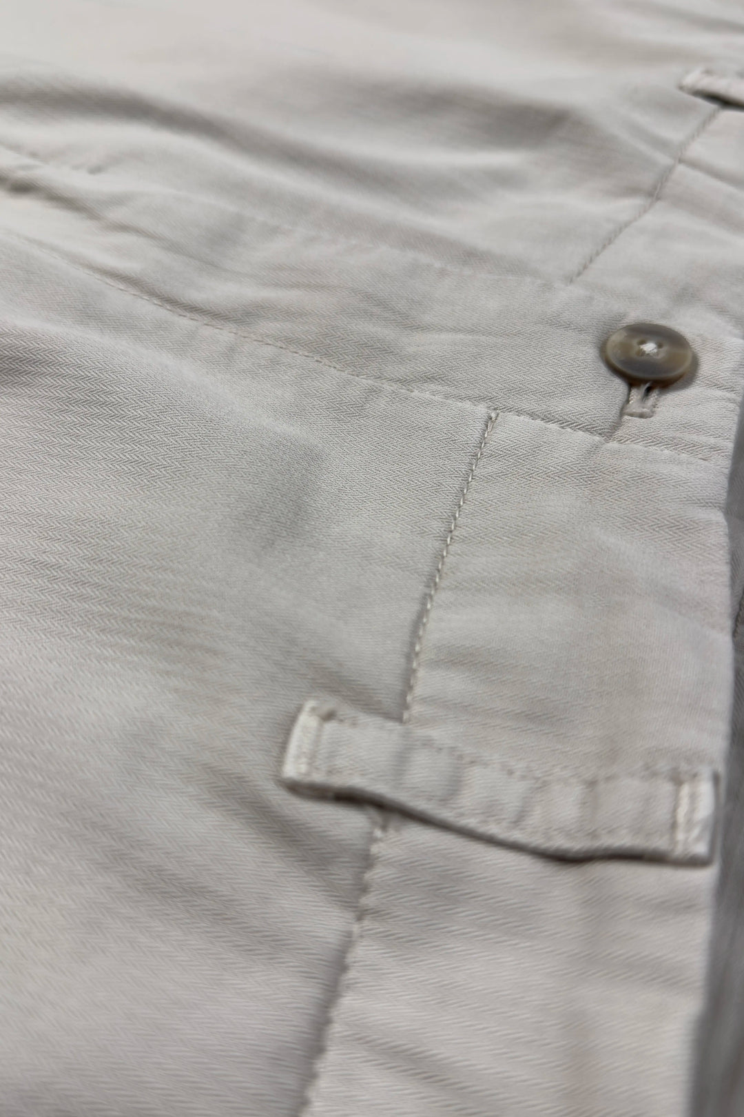 Close-up of light gray pants with a button and pocket detail.