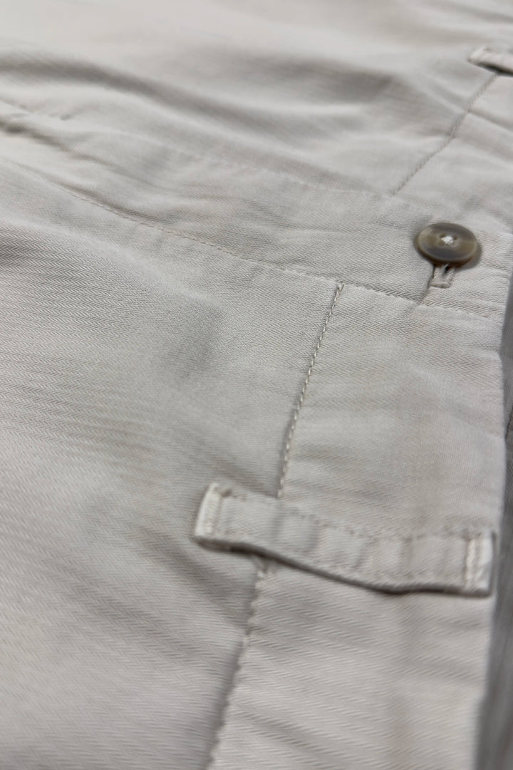 Close-up of light gray pants with a button and pocket detail.