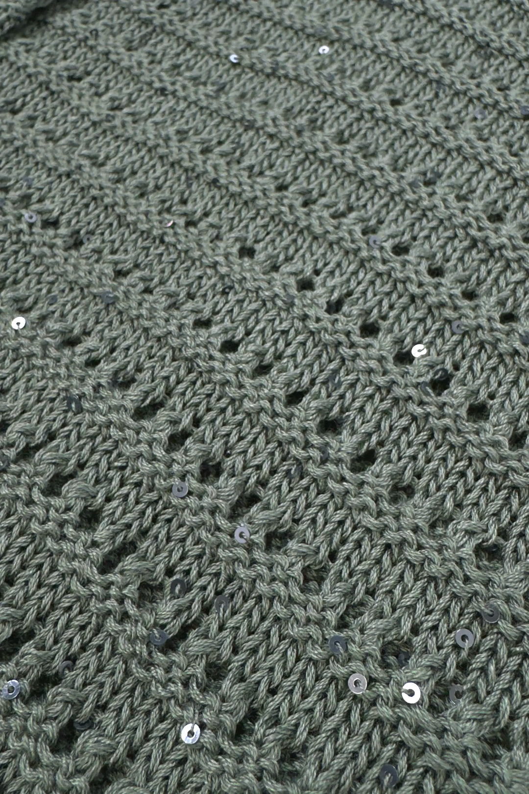 Close-up of a textured green fabric with a diamond pattern and small white beads.
