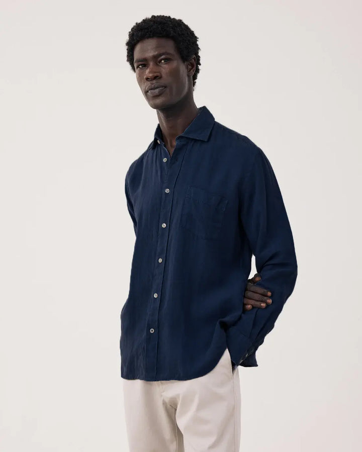 Man wearing a navy blue shirt and light-colored pants against a plain background