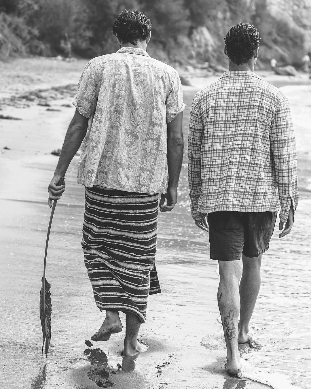 Two men walking along a beach, one holding a fishing net.