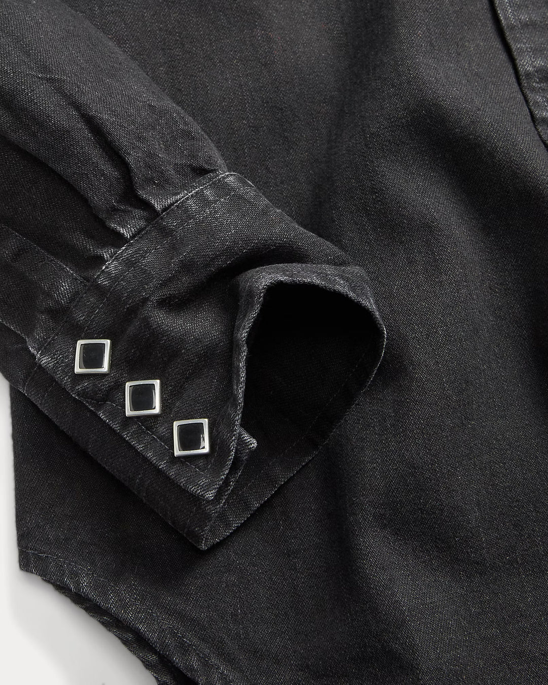 Close-up of a black shirt with rolled-up sleeve and decorative buttons on a white background