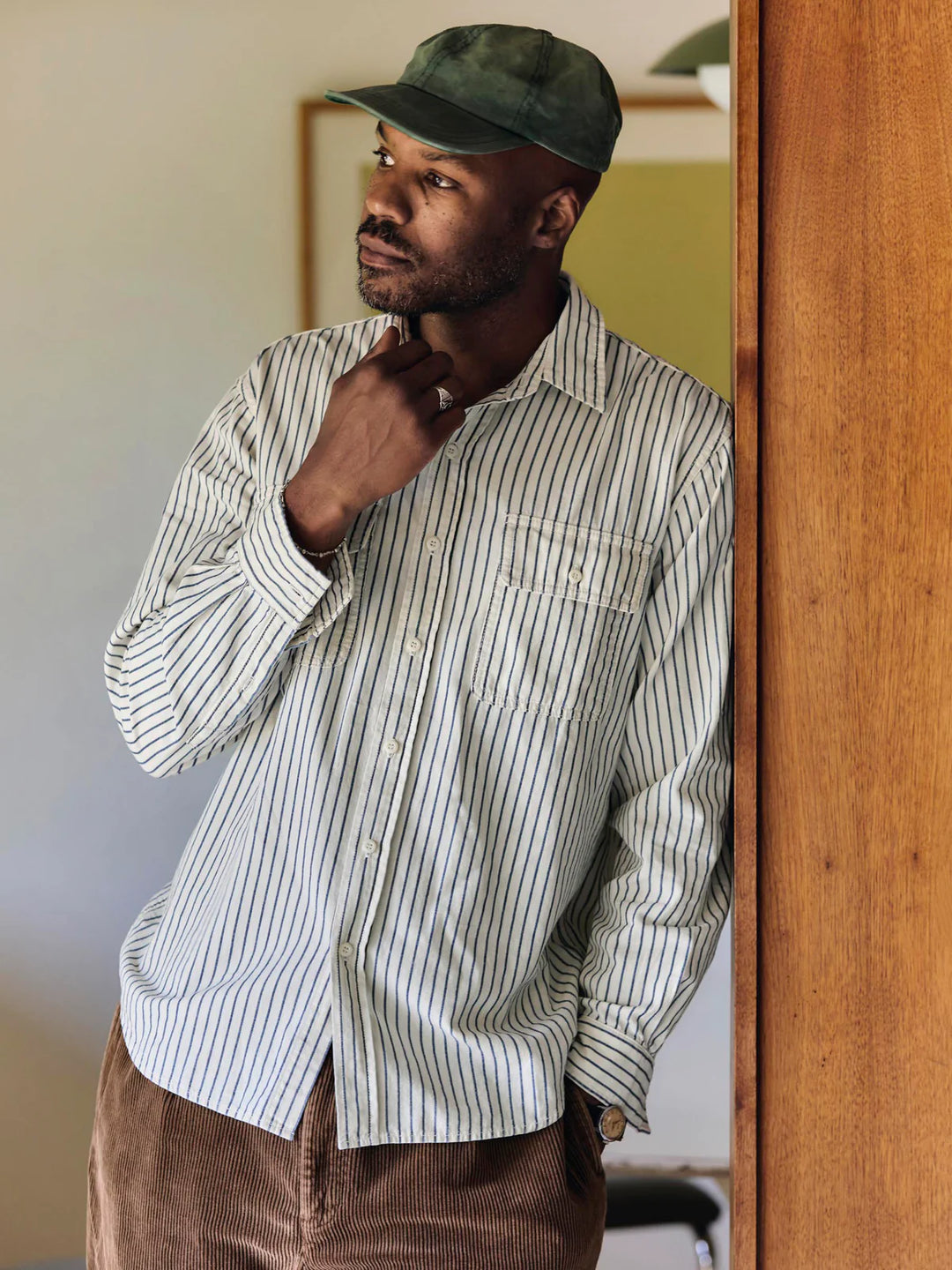 Man wearing a striped shirt and cap, standing indoors.