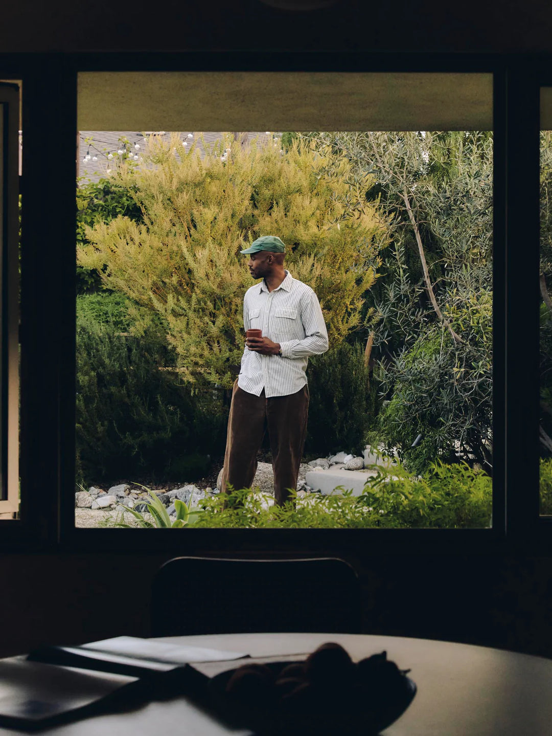 Man standing outdoors in a garden, looking out of a window.