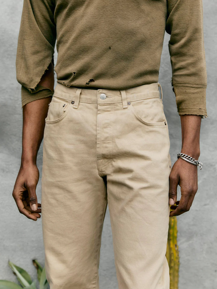 Person wearing a brown long-sleeve shirt and beige pants against a gray background