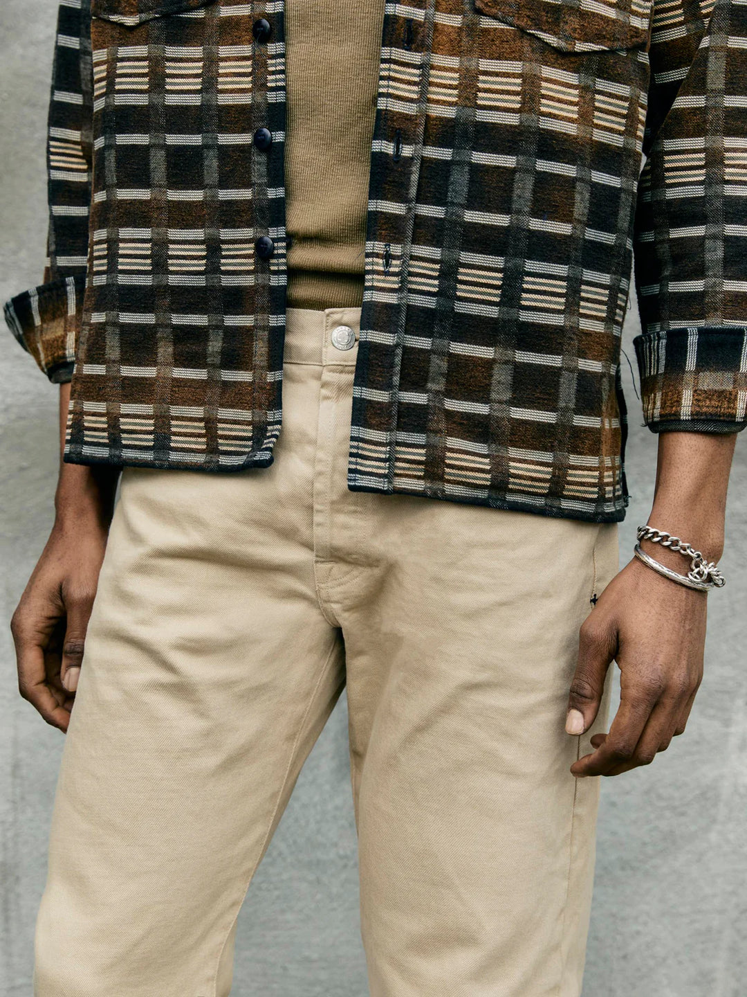 Person wearing a plaid shirt over a beige shirt with beige pants on a neutral background