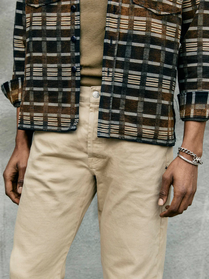 Person wearing a plaid shirt over a beige shirt with beige pants on a neutral background