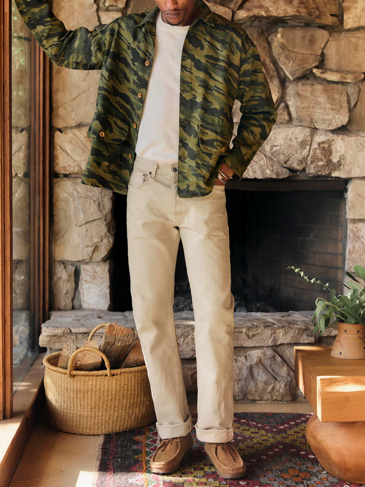 Person wearing a camouflage jacket and beige pants standing in front of a stone fireplace.