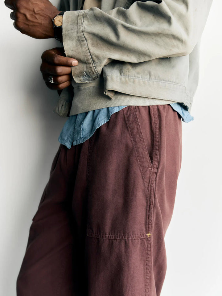 Person wearing a beige jacket over a blue shirt and brown pants on a plain background
