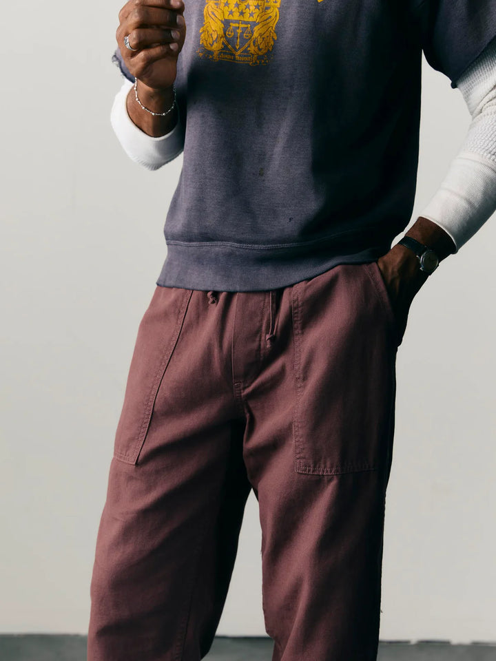 Person wearing a dark gray sweatshirt with a yellow logo and maroon pants against a plain background