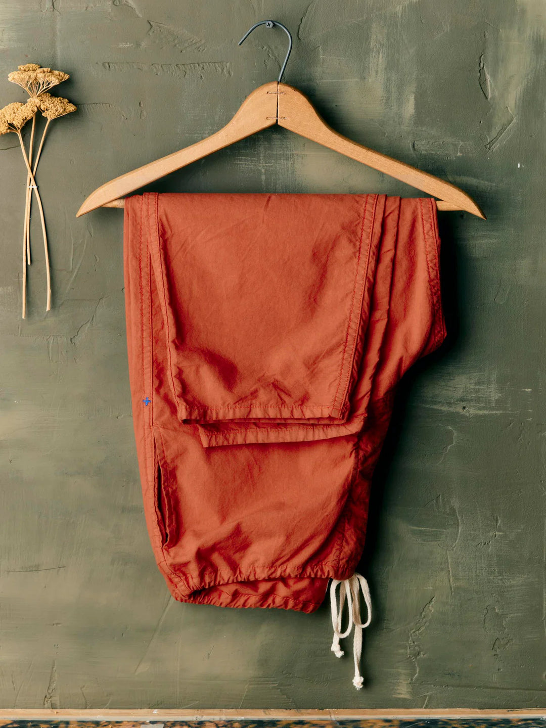Red pants on a wooden hanger against a textured green wall.