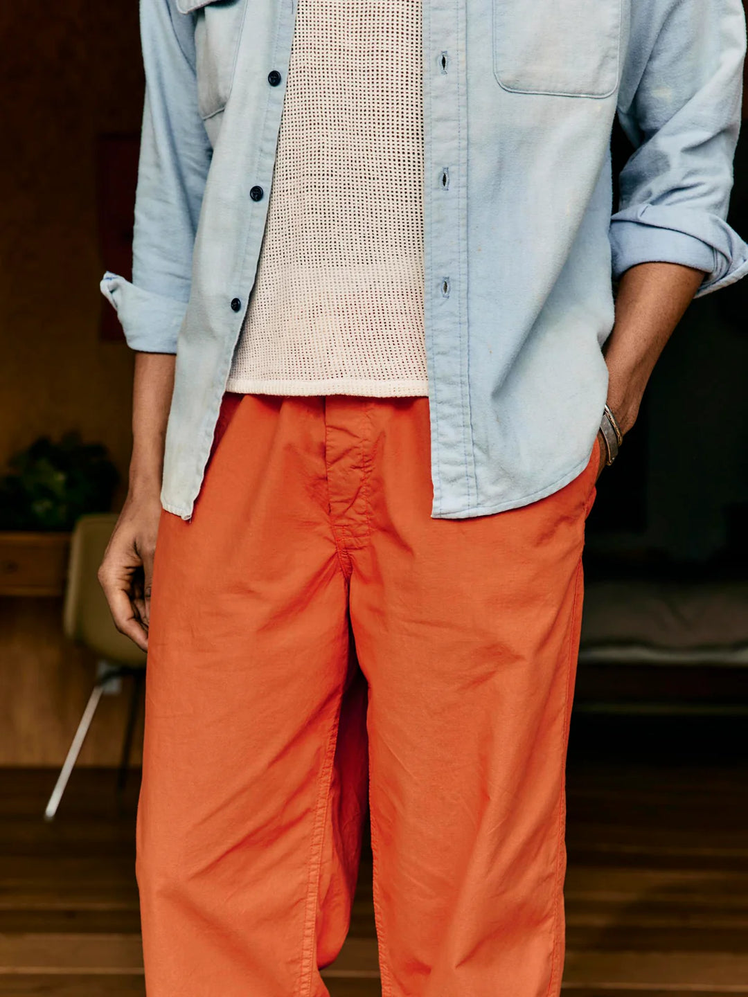 Person wearing a light blue shirt over a beige sweater with orange pants indoors.