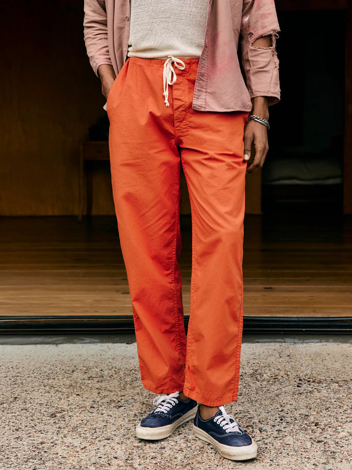Person wearing orange pants and a pink shirt standing on a gravel surface.