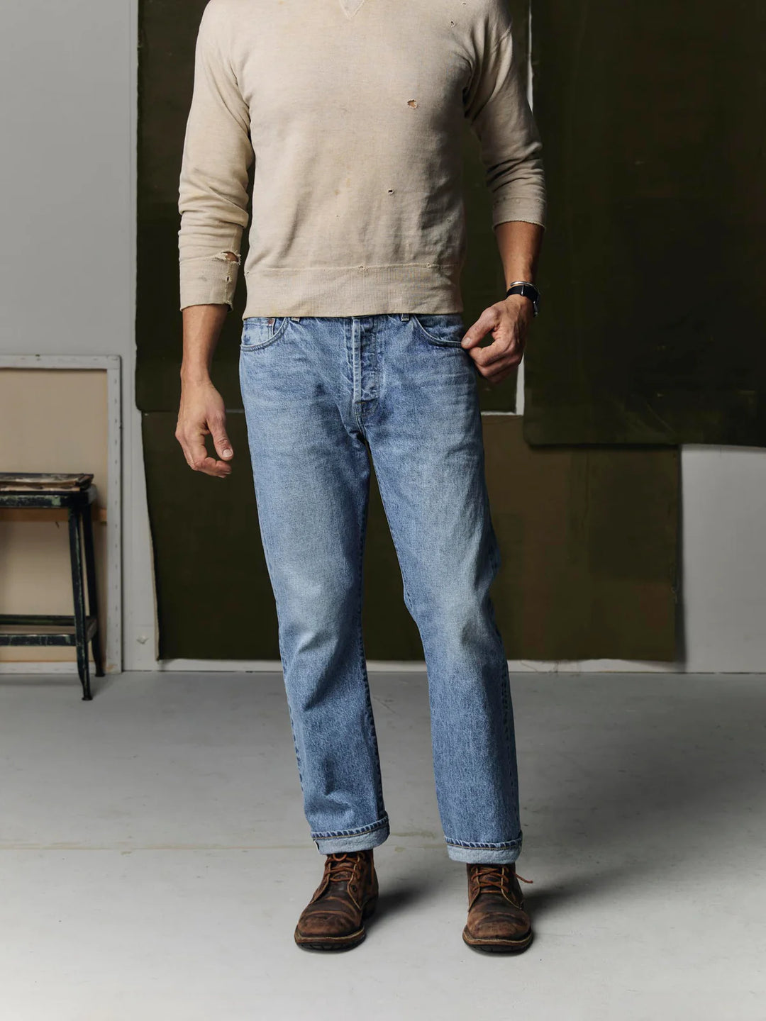 Person wearing a beige sweater and blue jeans standing indoors.