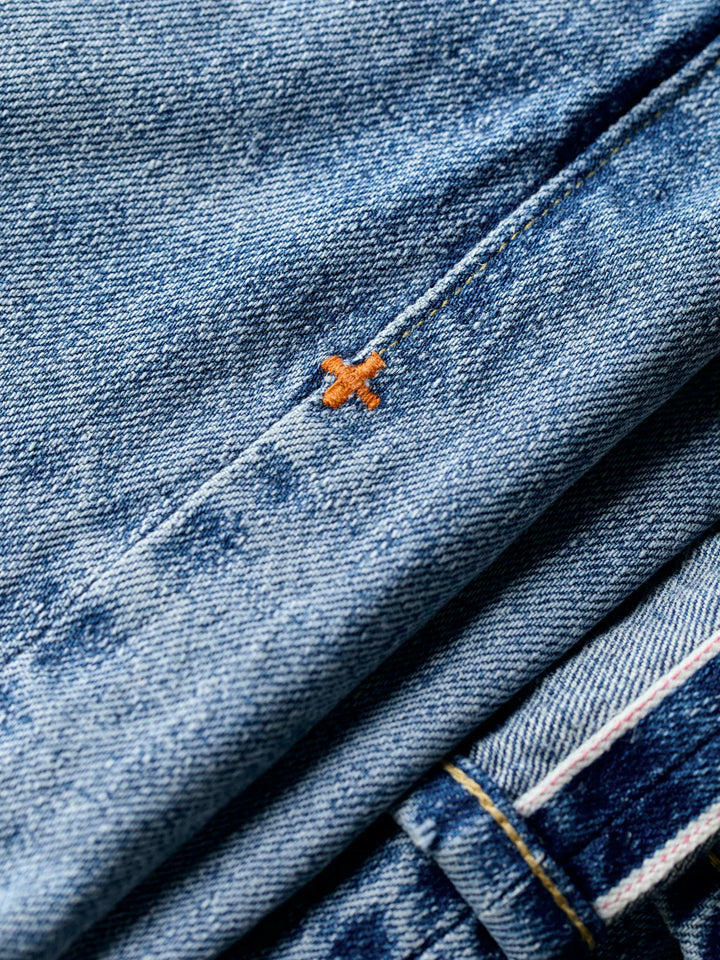 Close-up of blue denim fabric with a small orange cross on a black background