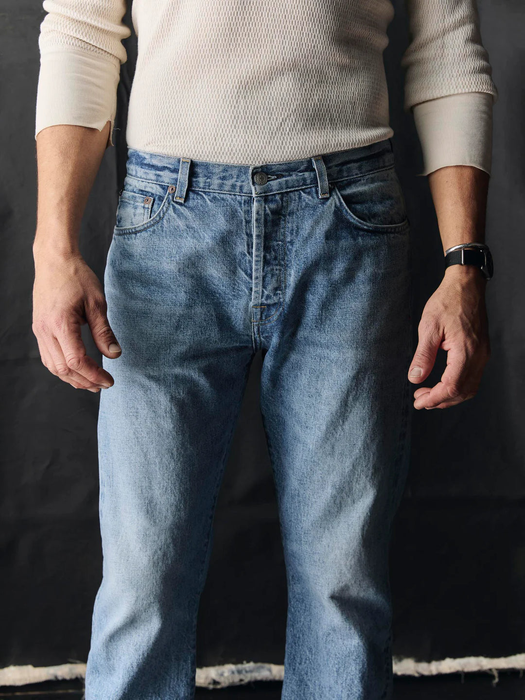 Person wearing light blue jeans and a cream sweater against a dark background