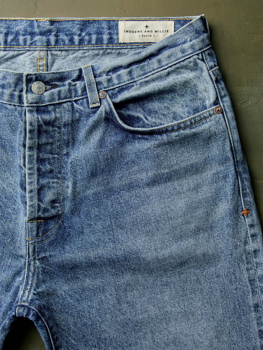 Close-up of blue jeans with a visible brand label on a green background