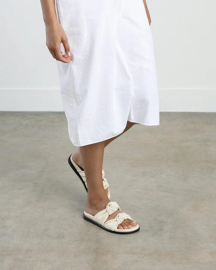 Person wearing a white dress and sandals on a plain background