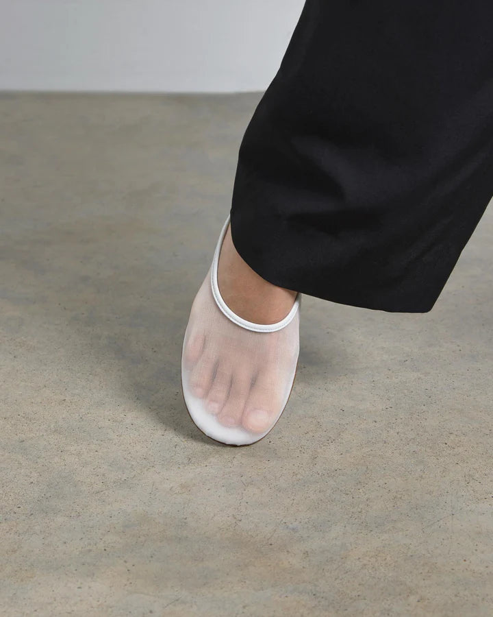 White sheer shoe on a gray floor with black pants